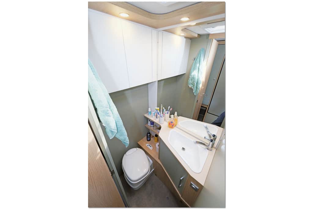 Nasszelle im LMC Style mit weißen und salbeigrünen Schrankfronten, dreieckigem Waschbecken, Chemietoilette und Oberlichtern