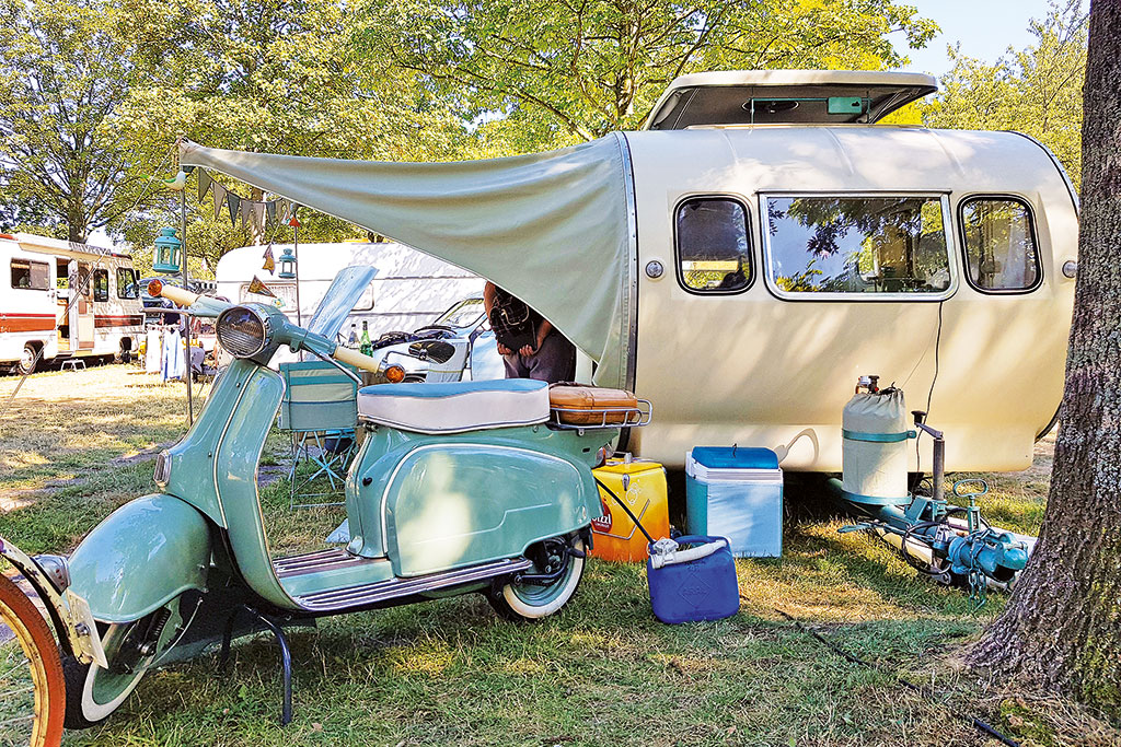Alter, cremefarbener Wohnwagen in Tropfenform und pastellblauer, alter Roller davor
