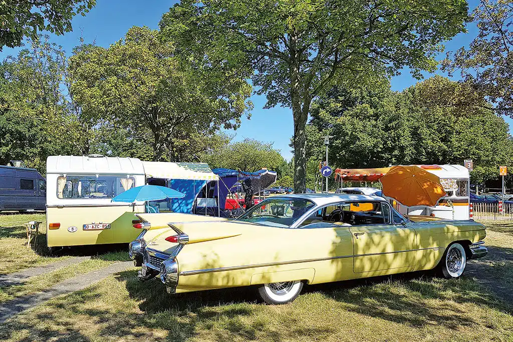 Pastellgelbes, altes Fahrzeug aus den USA mit daneben parkendem, farblich passendem alten Wohnwagen
