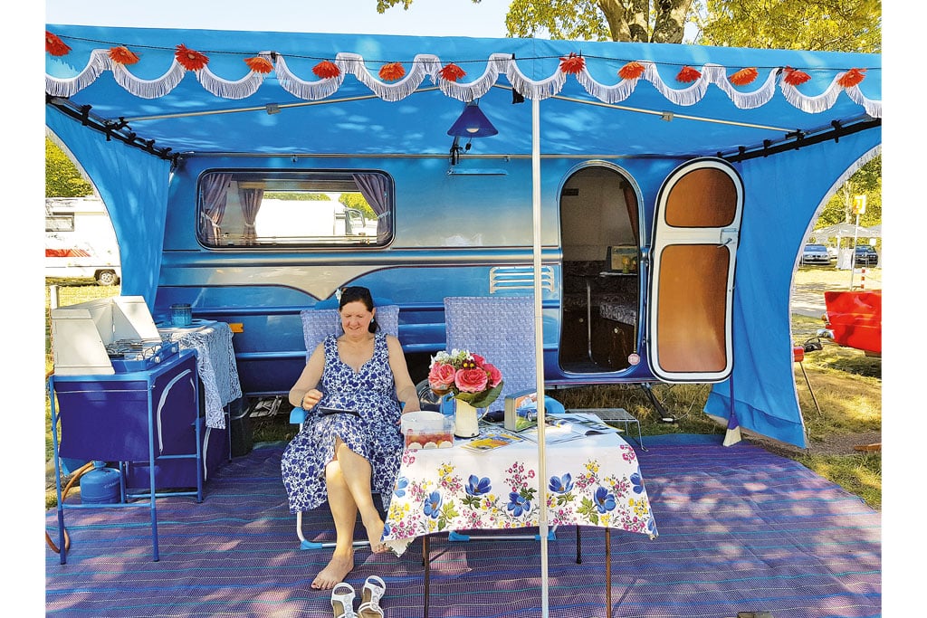 Teilnehmerin der Classic Days 2022 vor ihrem blau gestrichenen und blau dekorierten Wohnwagen.