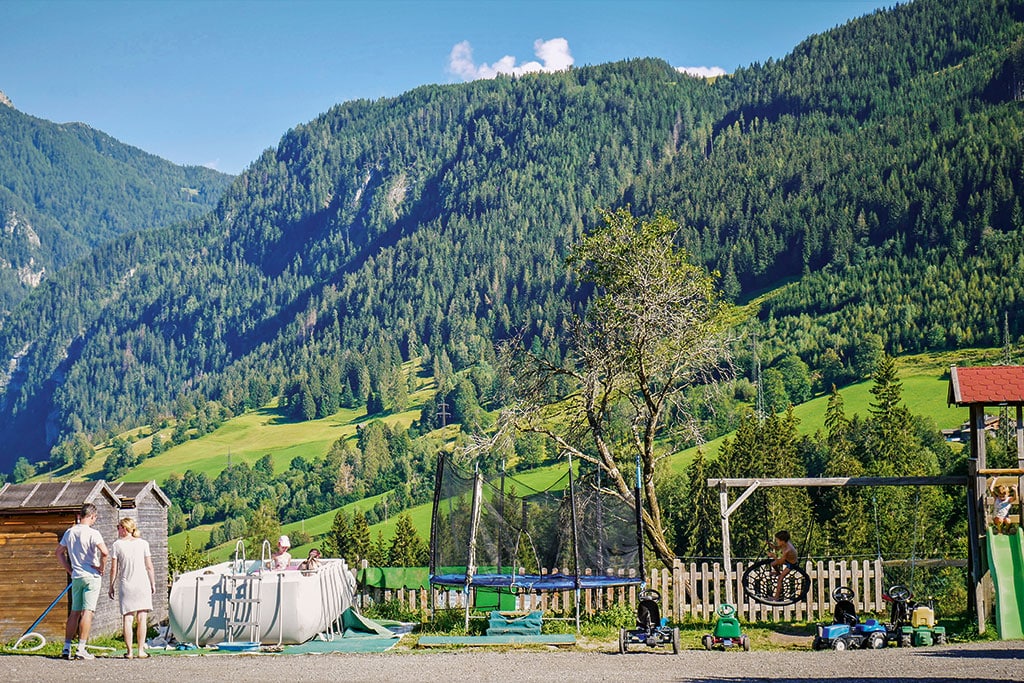 Spielplatz mit kleinem Pool, Trampolin und Schaukel in Alpenlandschaft