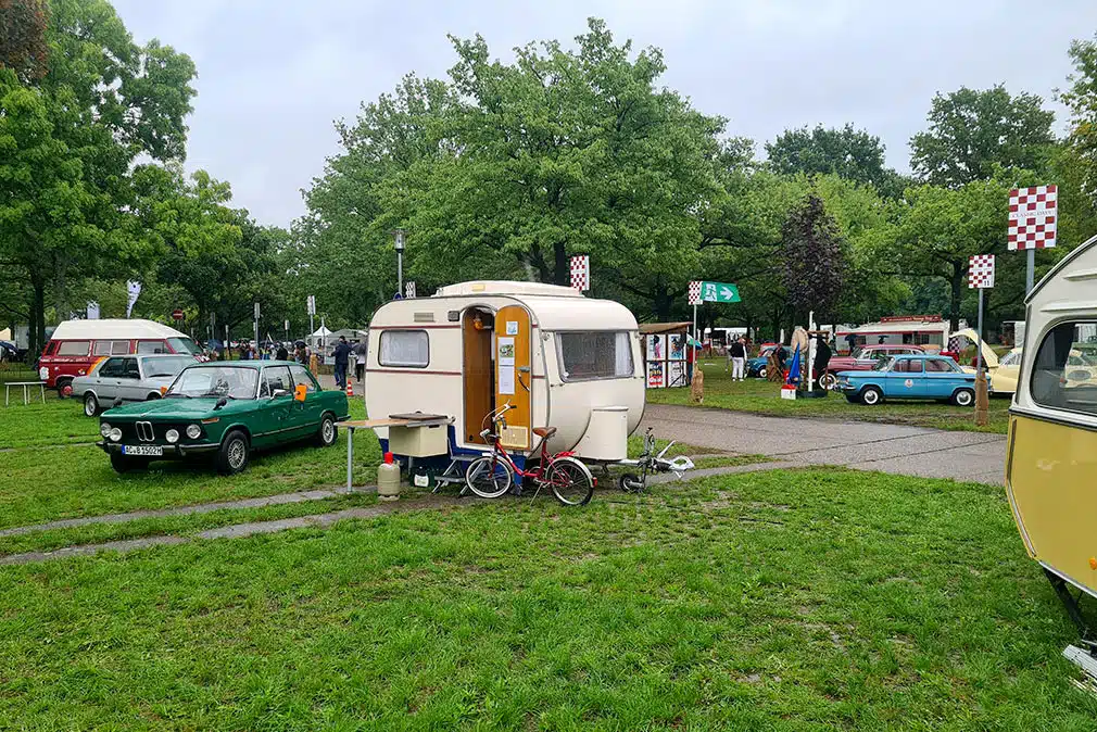 Kleiner, rundlicher Vintage-Wohnwagen und Oldtimer-Limousinen auf Parkgelände