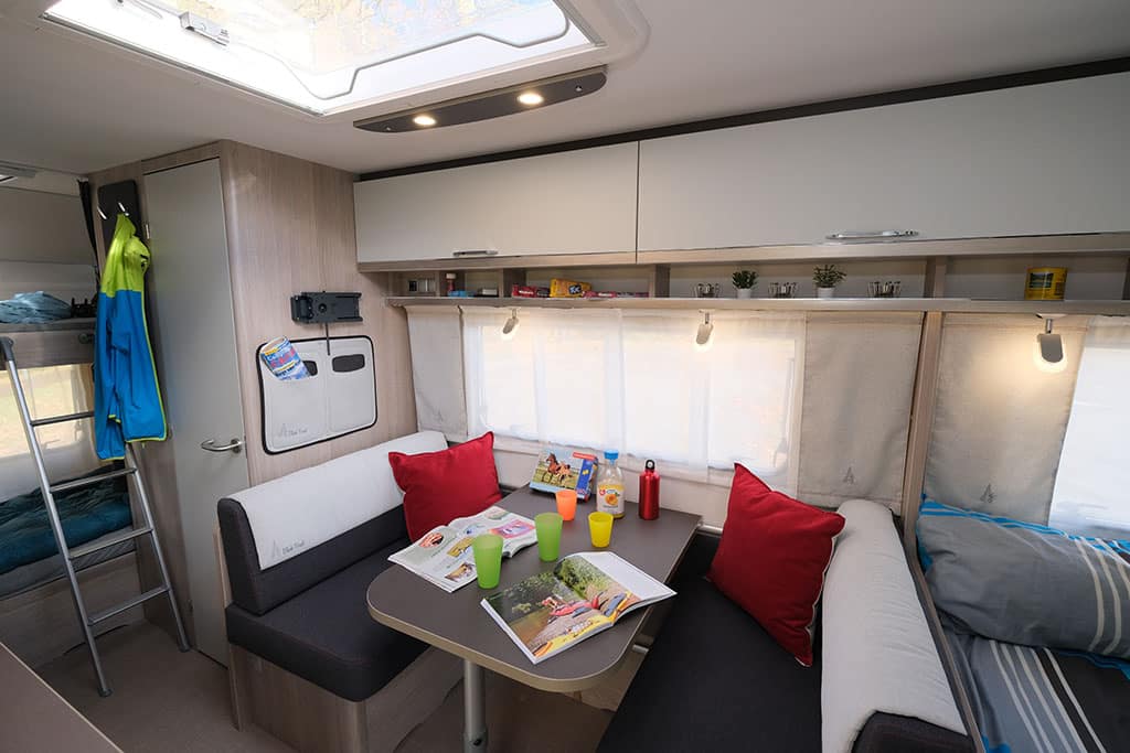 Zwei gegenüberliegende kleine Sitzbänke mit Tisch damitten im Wohnwagen