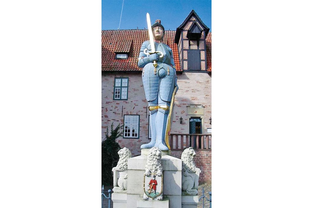 Steinerne Figur mit Schwert vor alter Burg