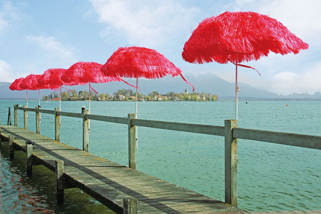 Rote Sonnenschirme säumen einen hölzernen Steg am Chiemsee