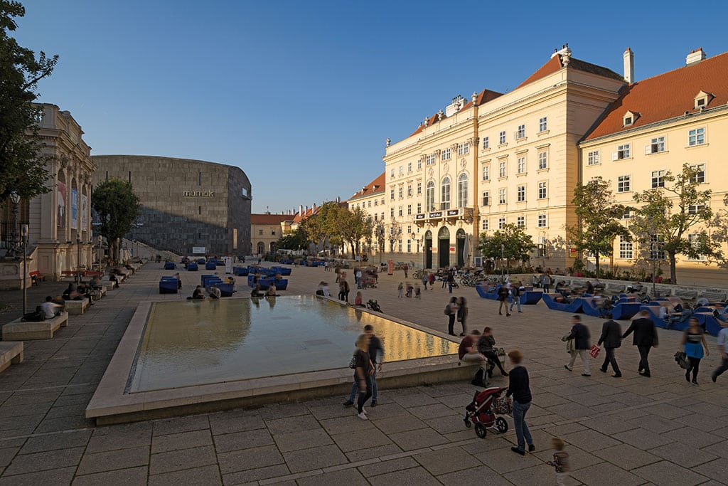 Großer Platz mit flaschem Brunnen, umgeben von alten Gebäuden