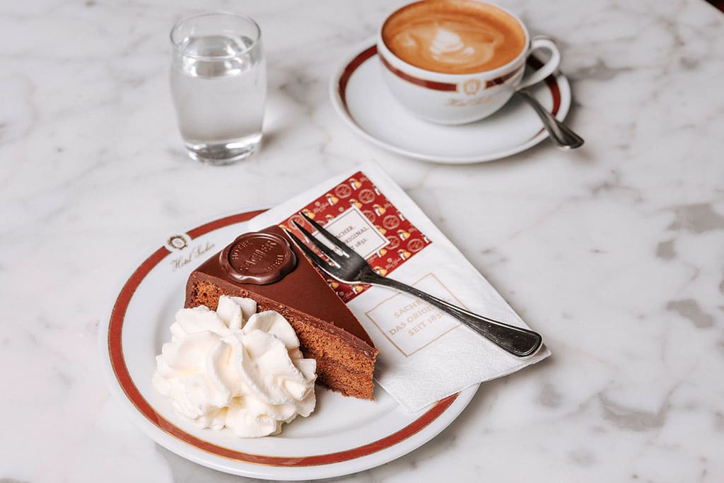 Ein Stück Sachertorte auf einem Teller und eine Tasse Kaffee