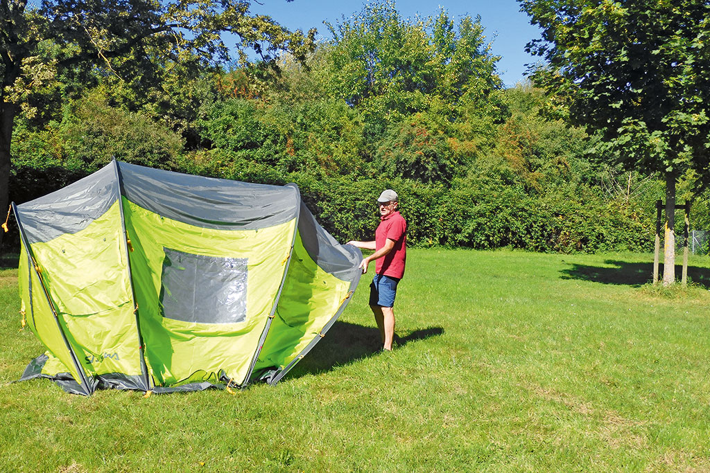 Mann stellt hellgrün-graues Tunnelzelt auf einer Rasenfläche auf