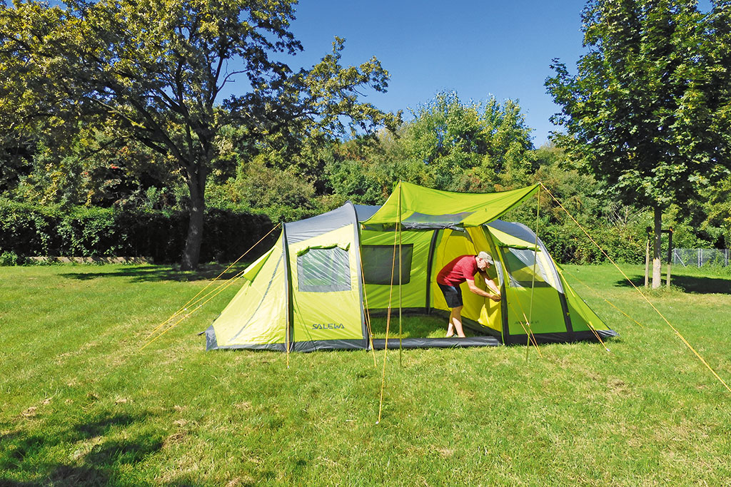 Mann montiert Innenzelt in einem hellgrün-grauen Tunnelzelt