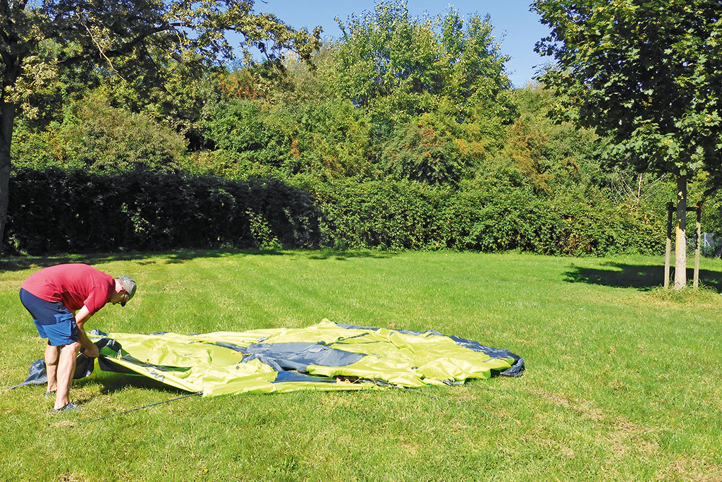 Mann neben auf einer Rasenfläche ausgebreiteten, hellgrünen Zelt