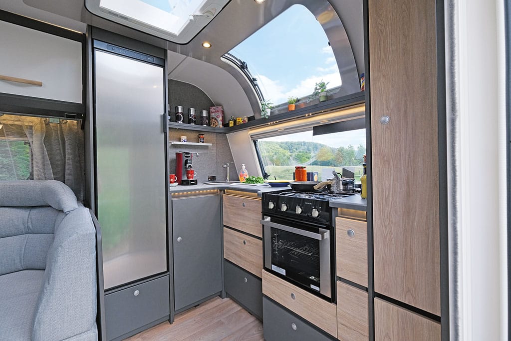 Große Wohnwagen-Küche mit großem Kühlschrank und Backofen, über der Küche ein großes Panoramafenster