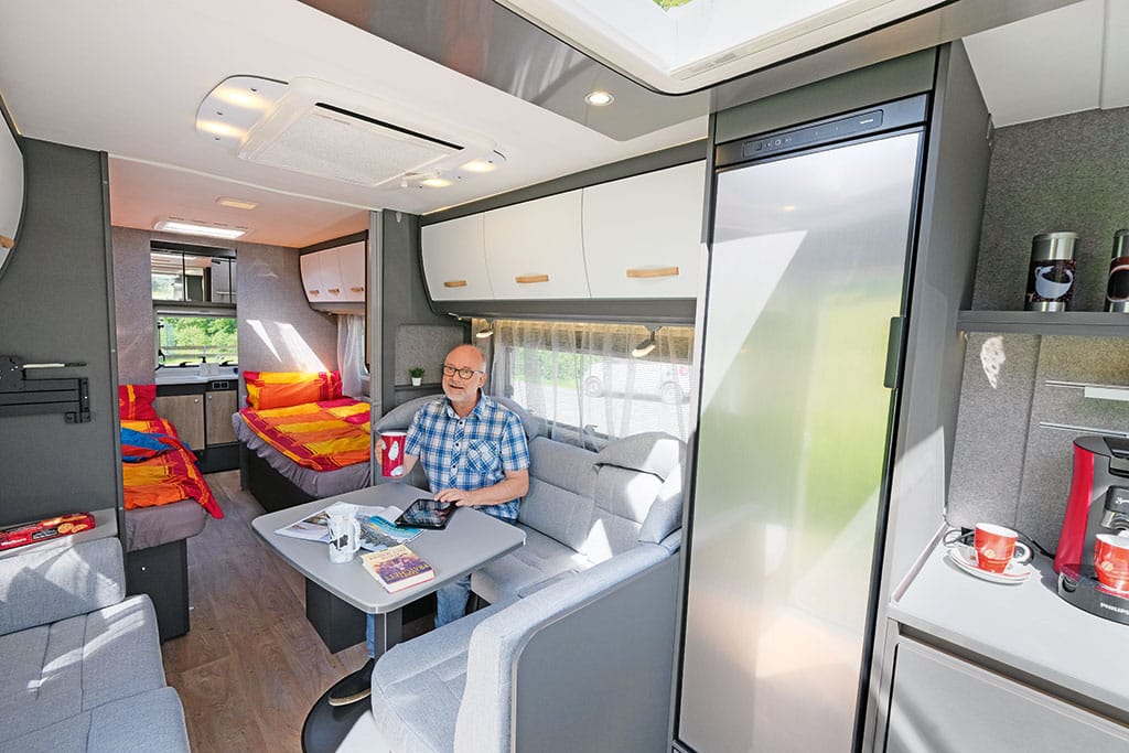 Mann auf einer grauen Polstersitzgruppe im Wohnwagen, dahinter ein Küchenmodul