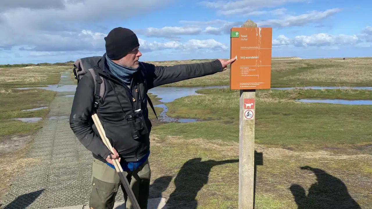 Ein Mann mit Mütze zeigt auf ein Schild mit Vorschriften.