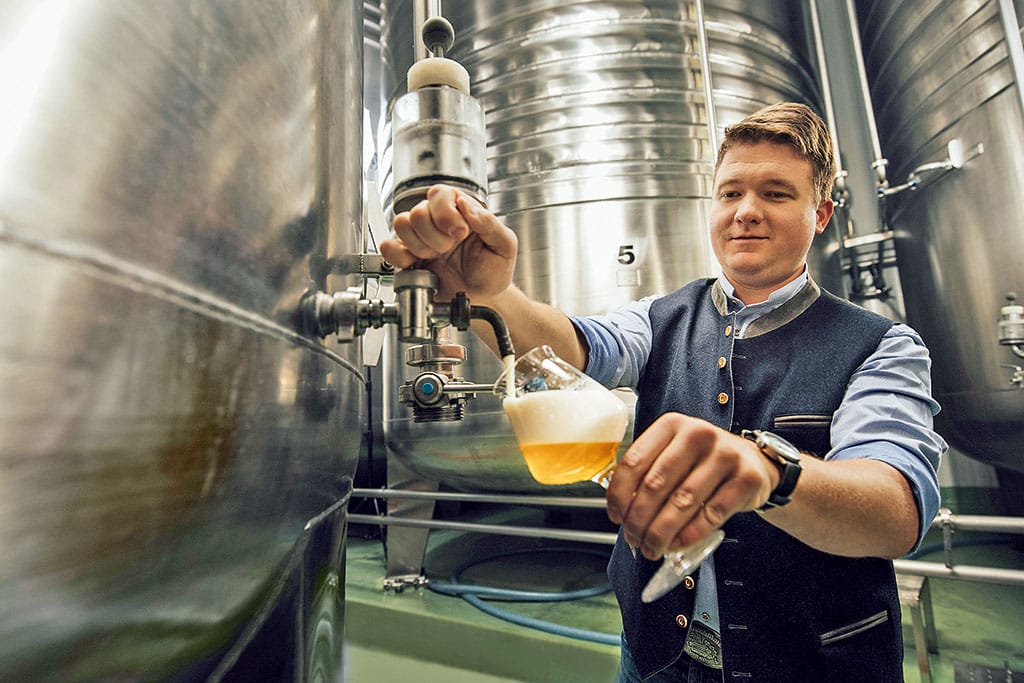 Mann zapft ein Glas Bier aus einem stählernen Tank in einer Brauerei
