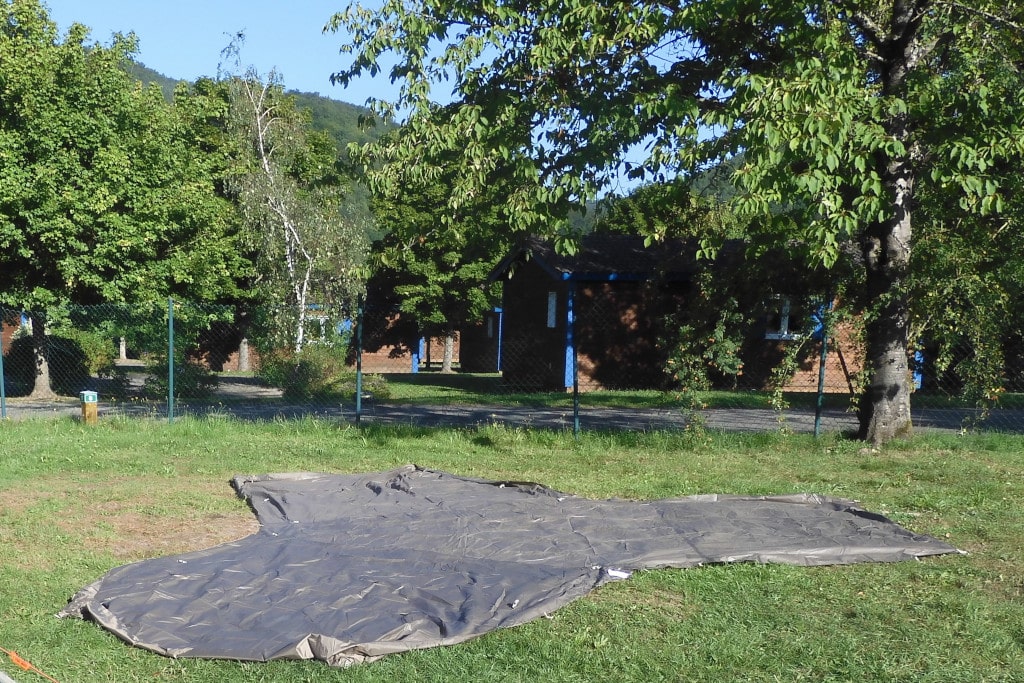 Ausgelegter grauer Zeltboden auf Wiese, in Grundform eines dreiblättrigen Kleeblatts.