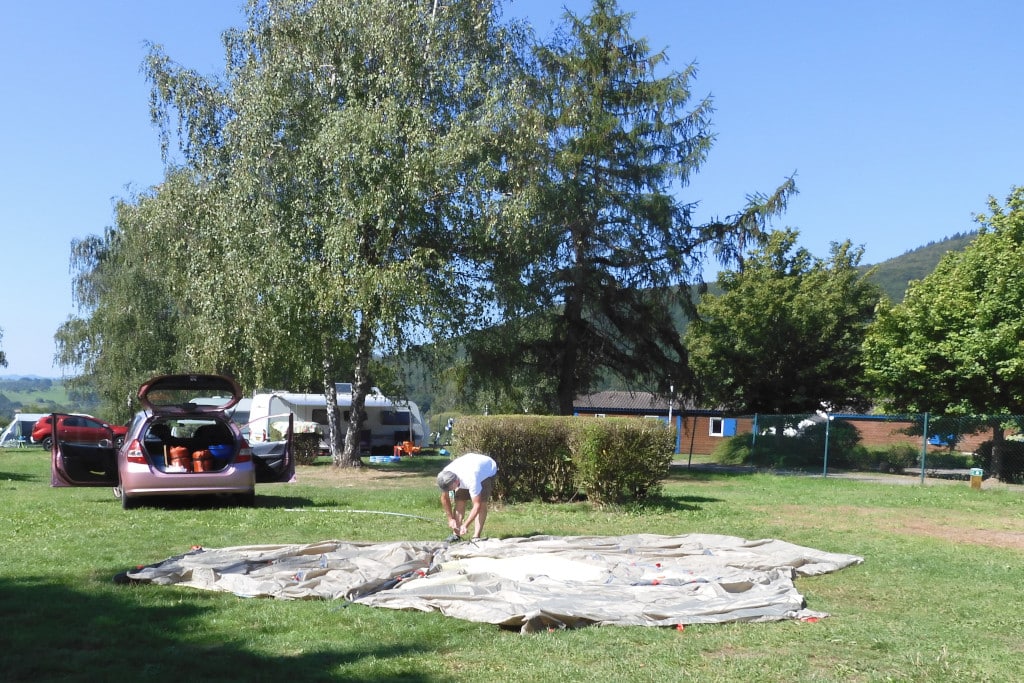 Mann baut Zelt auf Wiese auf und nutzt Zeltstangen.