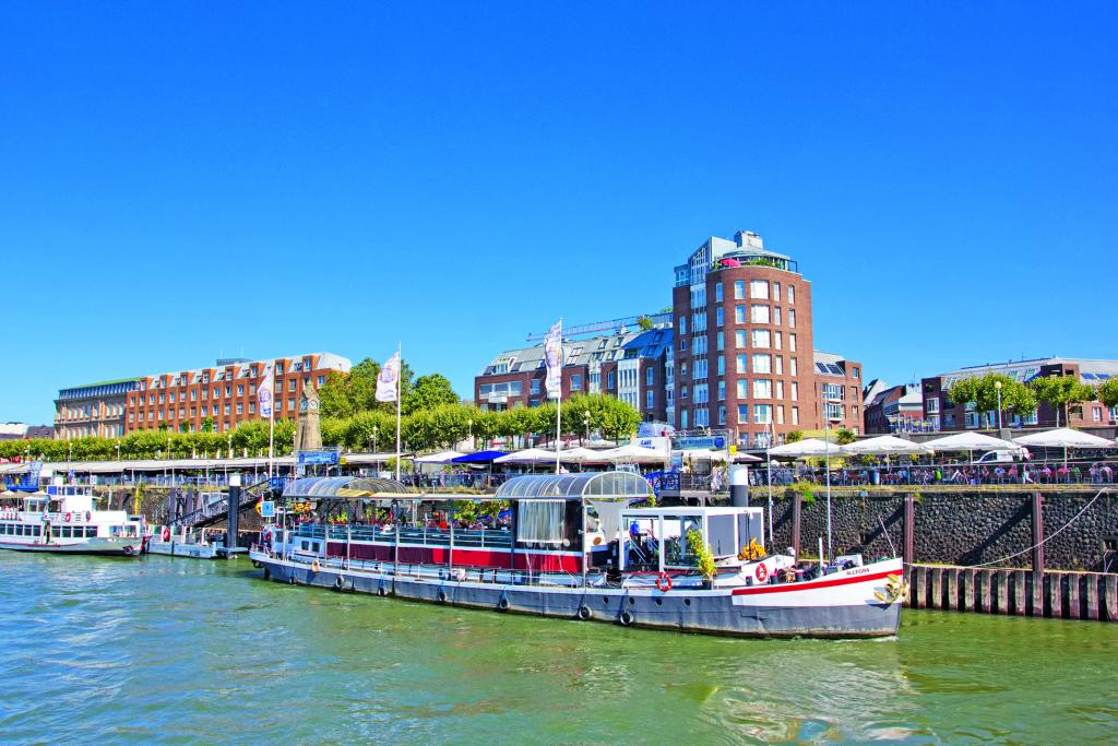 Ein Ausflugsschiff am Flussufer, im Hintergrund hohe Gebäude