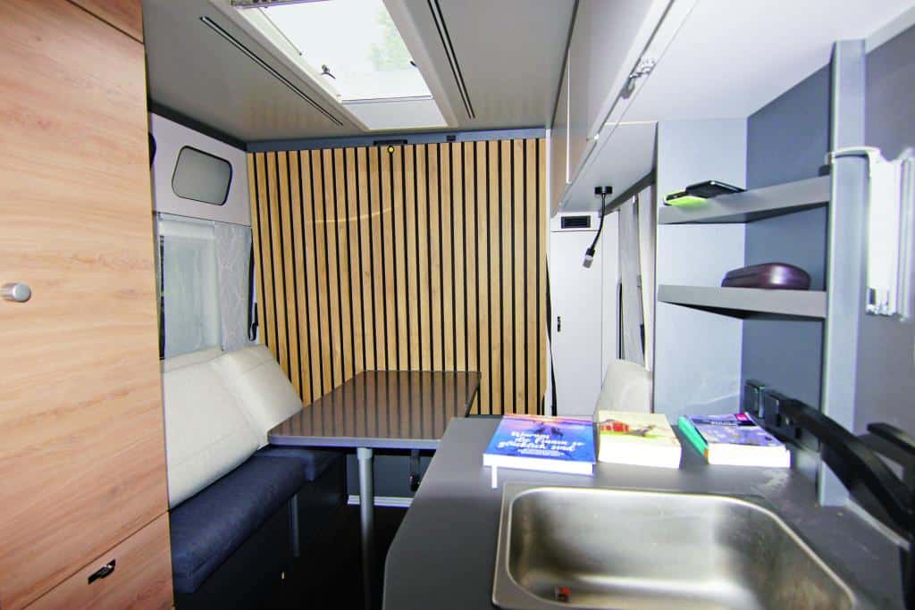 Wohnbereich im Wohnwagen mit Sitzbank, Tisch, Küchenmodul und Schränken.