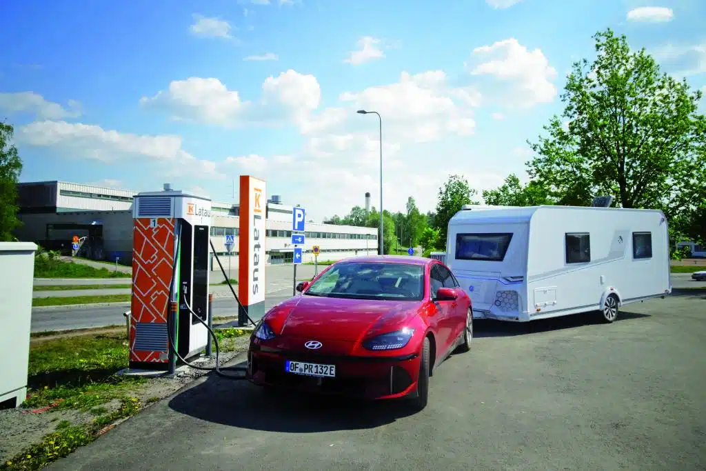 Rotes Auto mit weißem Anhänger an einer Strom-Ladesäule