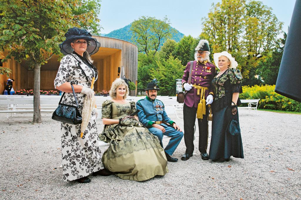 Drei Frauen und zwei Männer in aufwendiger, alter Tracht auf einem großen Platz umgeben von Bäumen