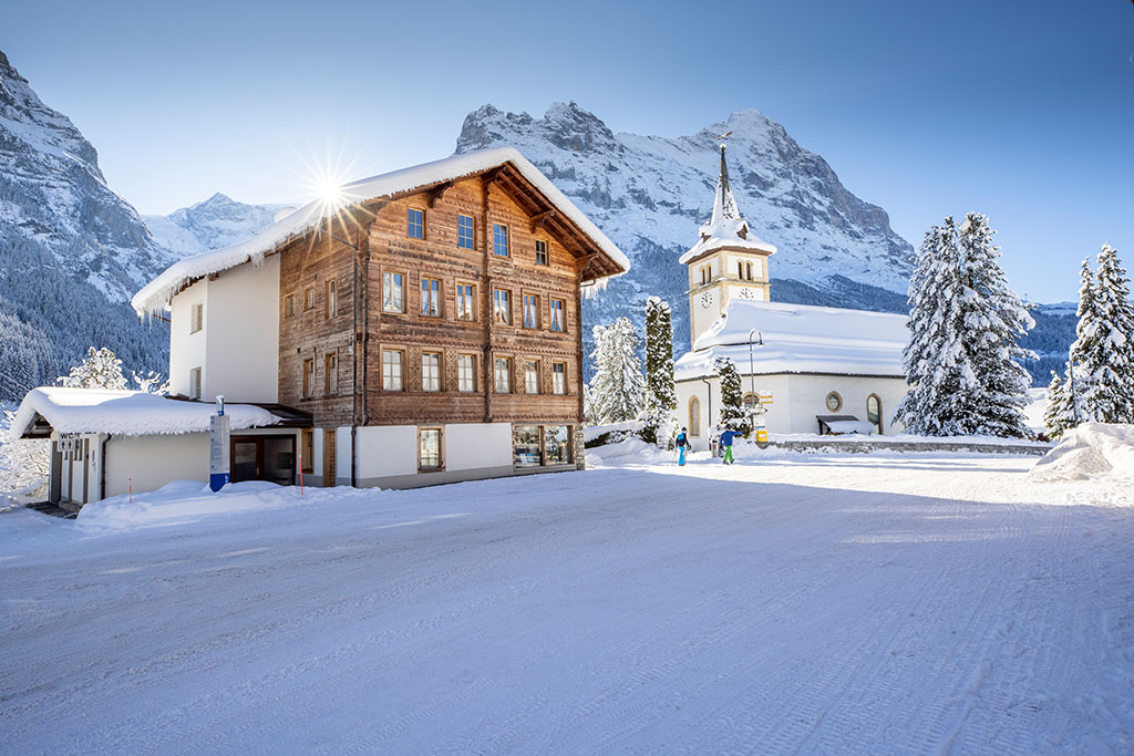 Eine Kirche und ein großes Gebäude mit teilweise Holzfassade in tief verschneiter Berglandschaft