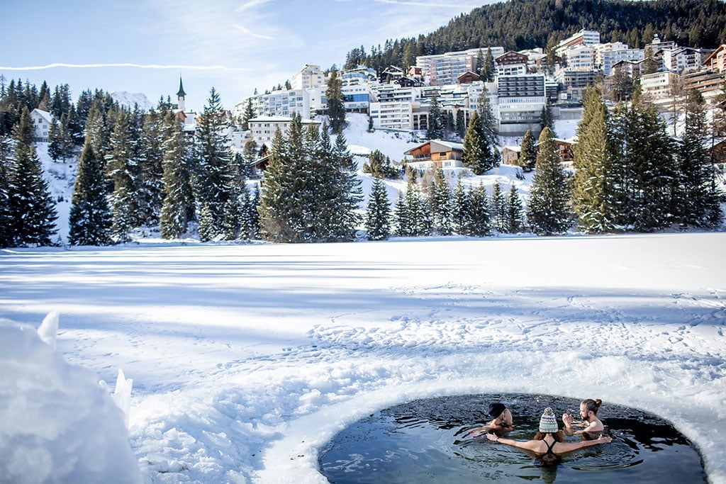 Einige Personen baden in einem kleinen, runden Teich inmitten verschneiter Landschaft