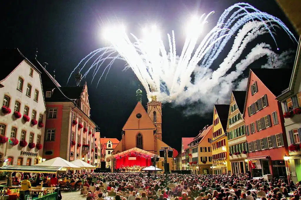 Viele Menschen auf einem zentralen Platz einer Stadt bei einem nächtlichen Feuerwerk