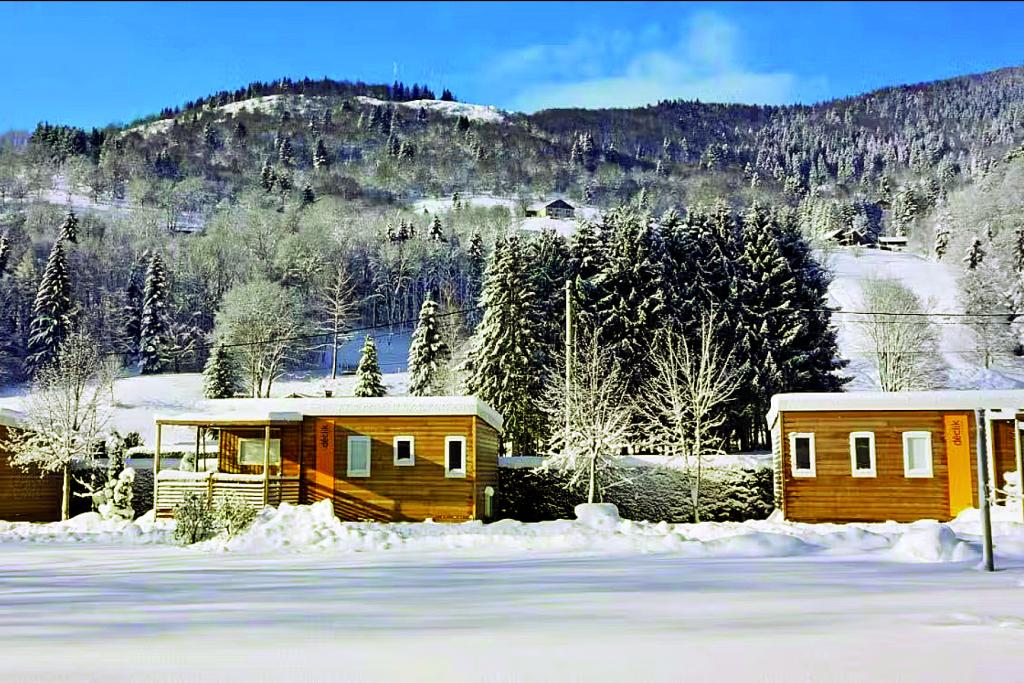 Zwei kleine Holzhütten auf einem Campingplatz in verschneiter Berglandschaft