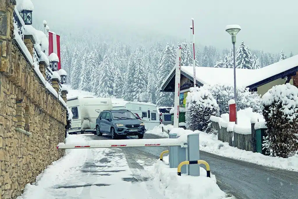 Ein Wohnwagen-Gespann fährt auf einer Auffahrtstraße aufs Gelände eines Campingplatzes in schneebedeckter Winterlandschaft