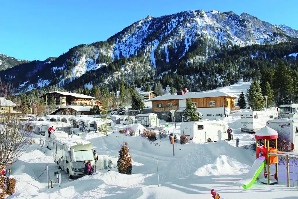 Campingplatz mit Kinderspielplatz im Winter in verschneietr Alpenlandschaft