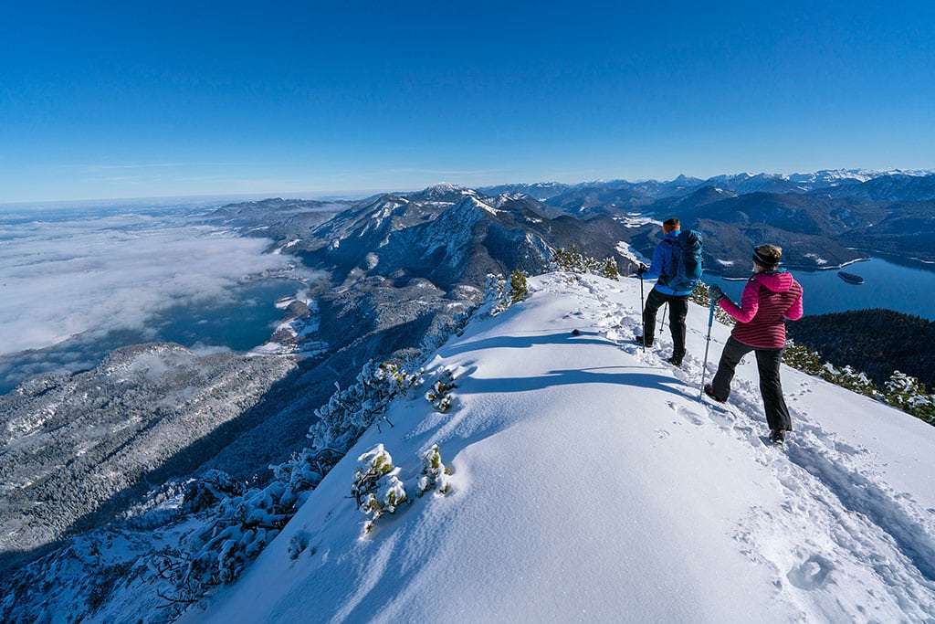 Zwei Winterwanderer auf einer Bergkuppe in verschneiter Berglandschaft