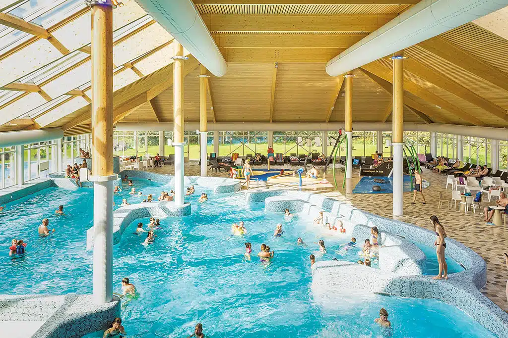 Viele Menschen in einer großen Indoor-Swimmingpool-Halle mit Sandbereich am Rand