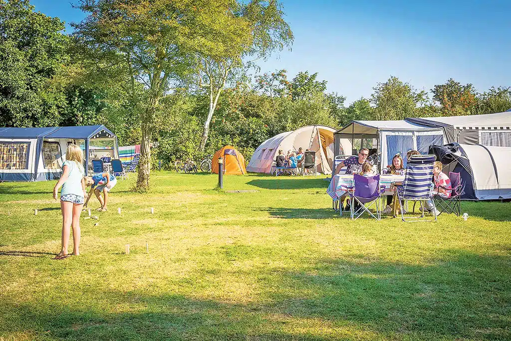 Spielende Kinder und einige Erwachsene am Campingtisch auf einem Campingplatz