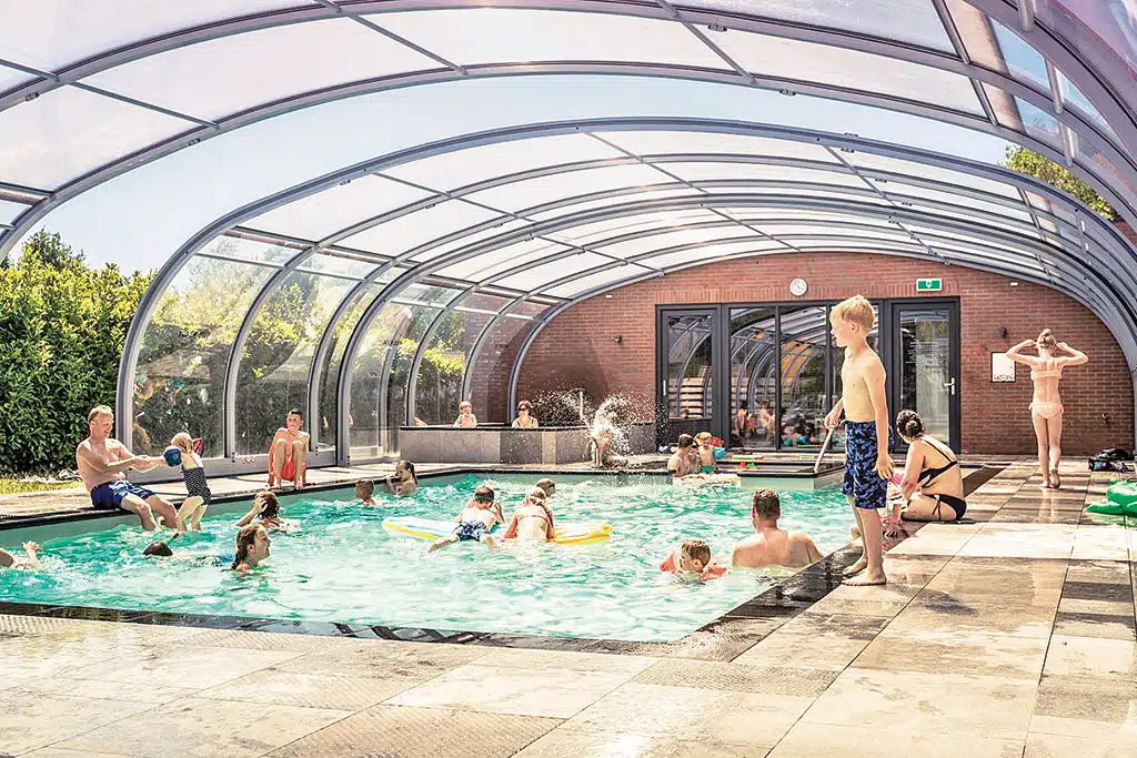 Kinder und Erwachsene in einer Indoor-Pool-Halle mit Runddach aus Glas