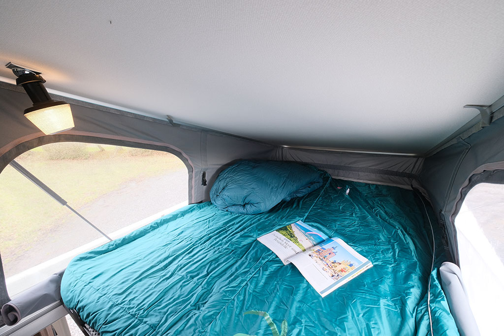 Schlafbett im Eriba Touring 620 mit blauer Bettdecke und Magazinen darauf.