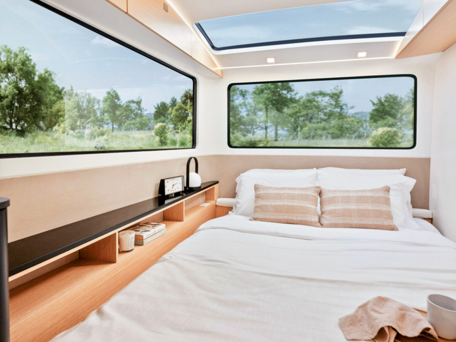 Bett im Wohnwagen, mehrere große Seiten- und Dachfenster erhellen den Raum deutlich