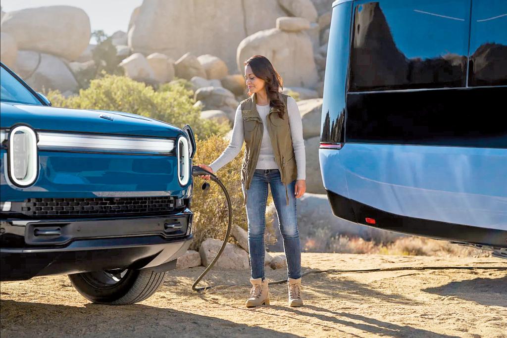 Eine Frau verbindet ein Stromkabel zwischen dem Pebble Flow-Caravan und einem Auto.