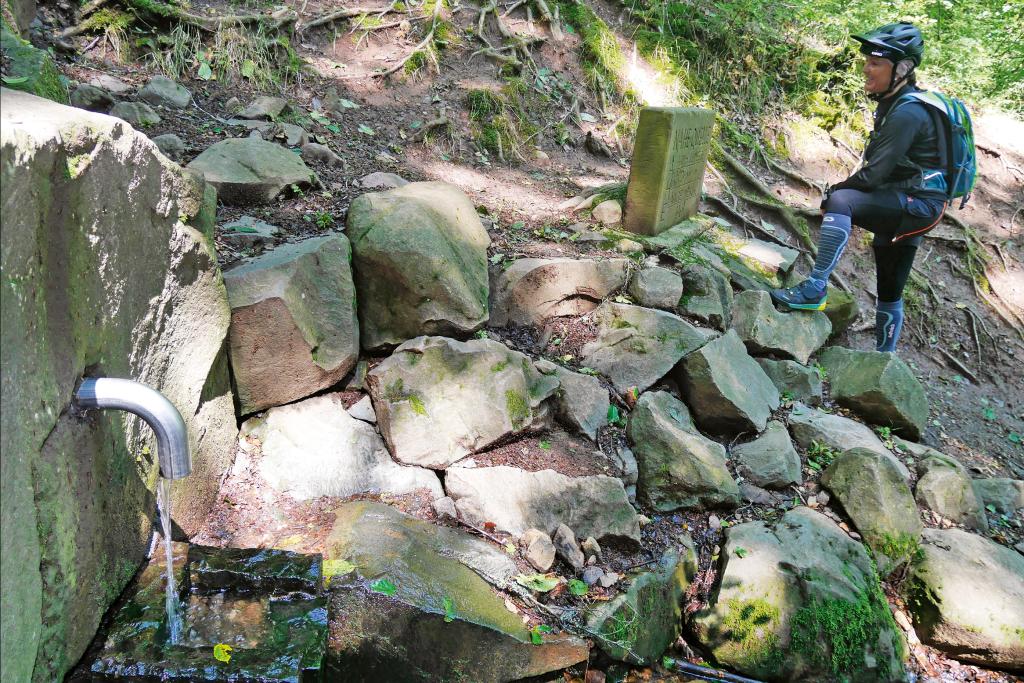 Wasser läuft aus einem Rohr über Felsen hinab, daneben steht ein Mann